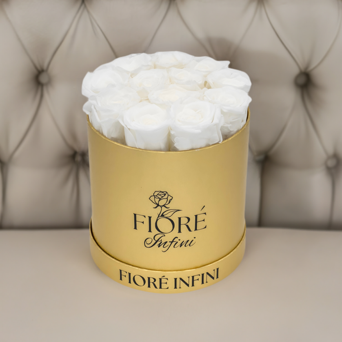 12 white forever roses in a gold foil box on a tan sofa