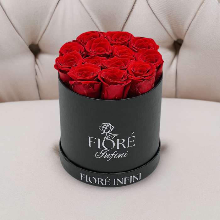 12 red forever roses in a black round box on a tan sofa